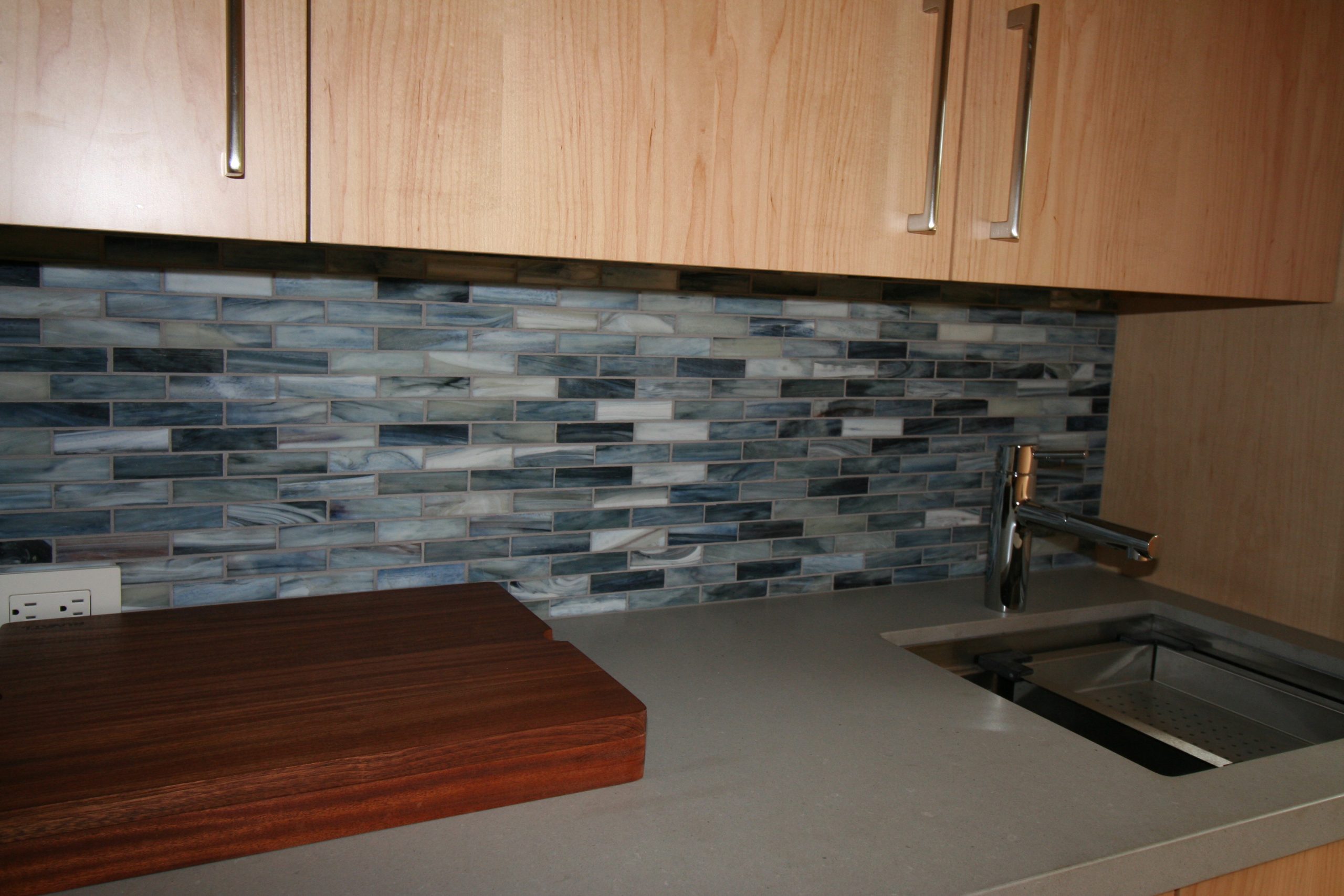 Ocean blue glass mosaic backsplash adds elegance to this mini bar. Custom glass tile installation for a modern touch.
